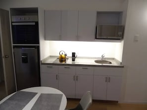 A compact kitchen with a refrigerator, microwave, sink, and a small dining table.