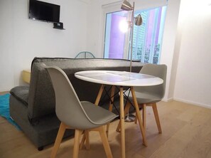 A living room with a sofa, two chairs, a small table, a TV, and a window with blinds.