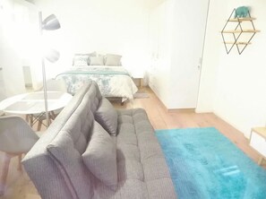 A modern bedroom with a grey sofa, a bed with patterned bedding, a blue rug, and a geometric wall decoration.