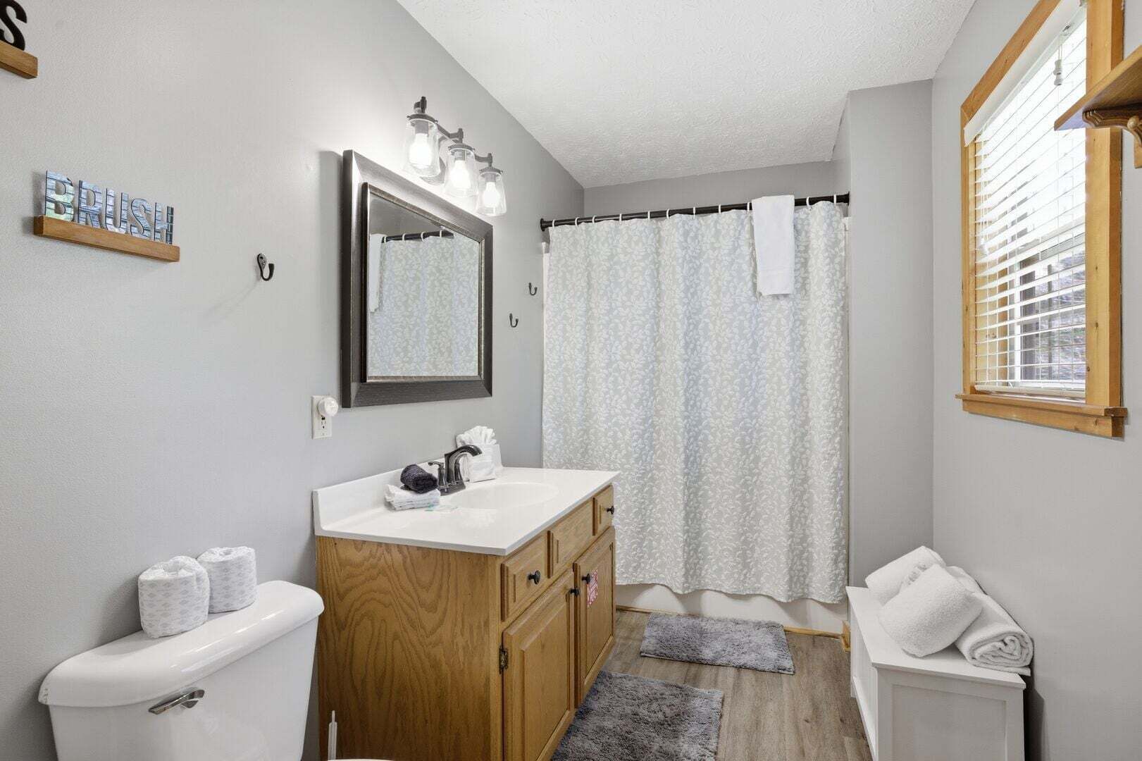 Une salle de bain avec un meuble-lavabo en bois, un miroir, un rideau de douche et une fenêtre.