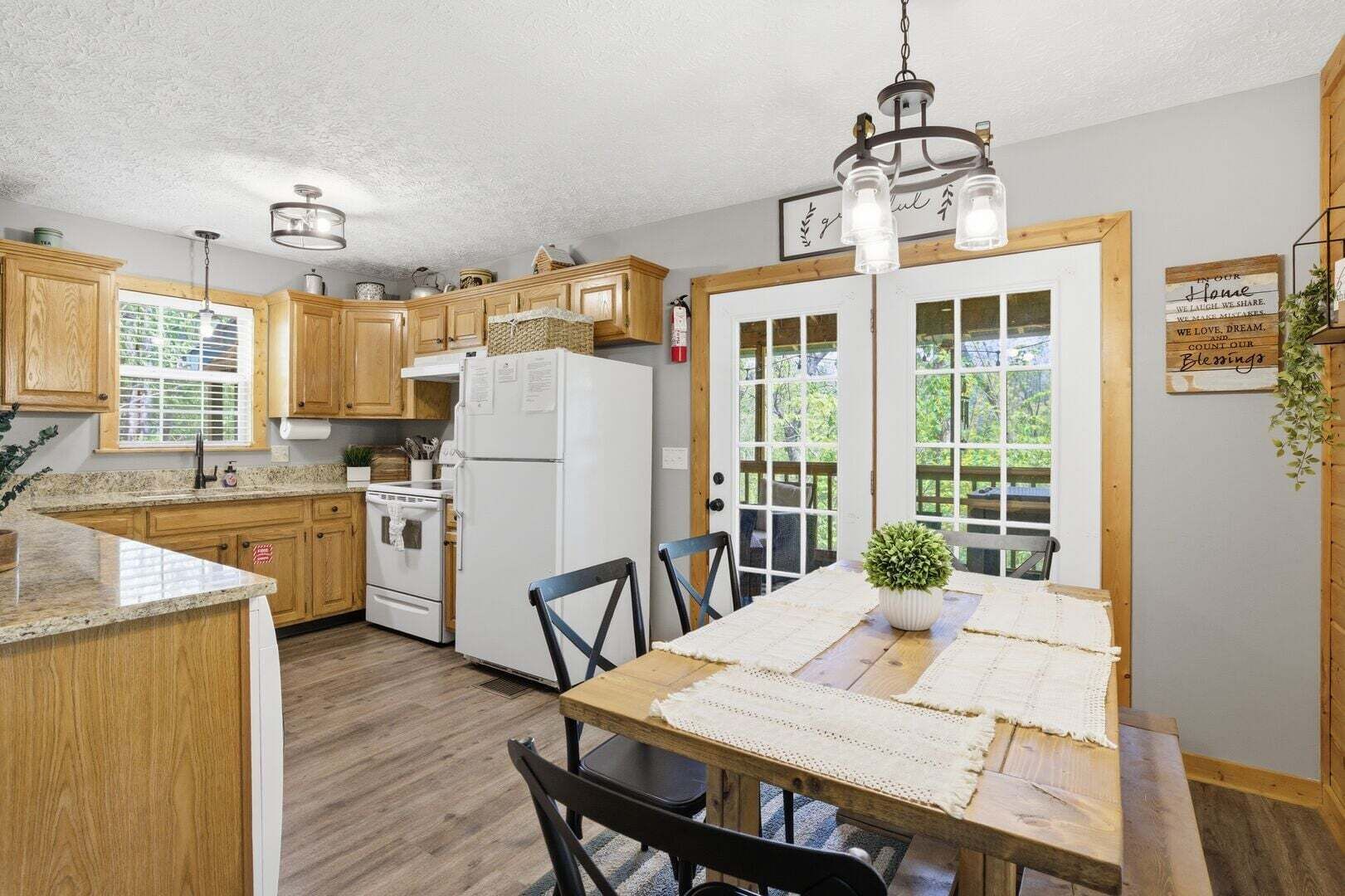 Une cuisine avec des meubles de rangement en bois, un réfrigérateur blanc, une table à manger avec des chaises et un luminaire suspendu.