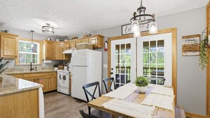 Una cocina con armarios de madera, un refrigerador blanco, una mesa de comedor con sillas y una lámpara colgante.