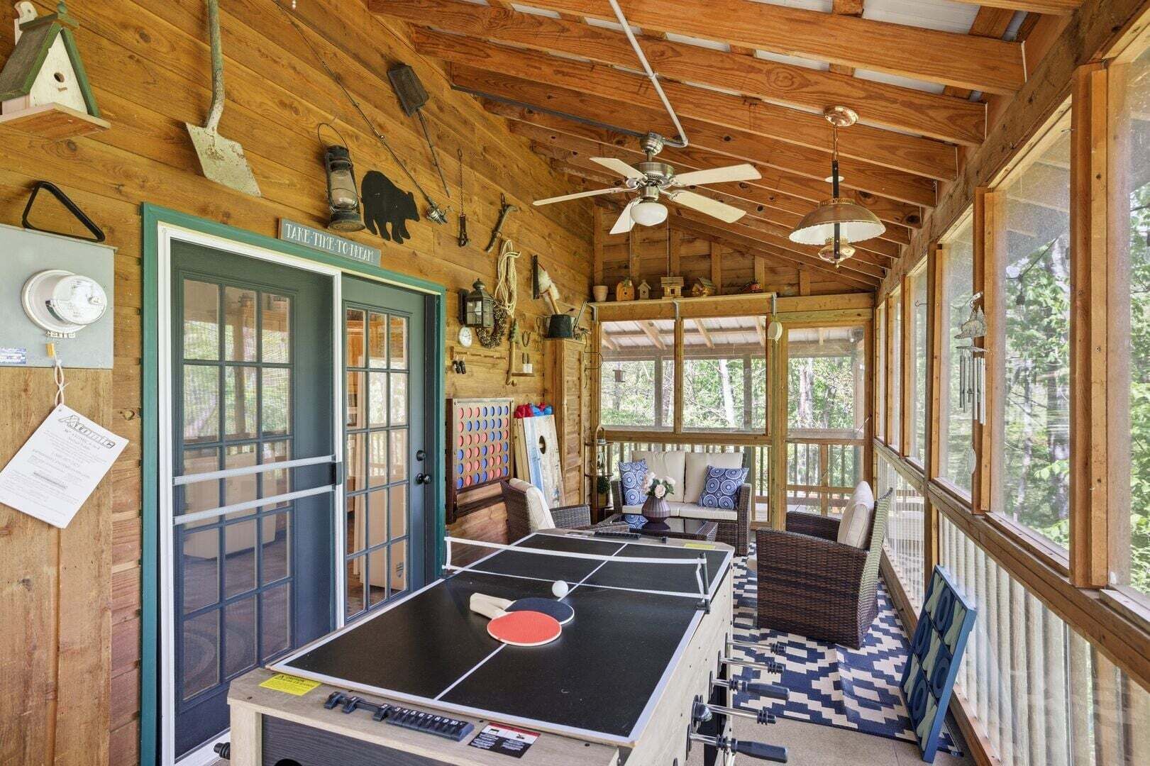 A wooden cabin with a ping pong table, a door with a sign, and a large window.