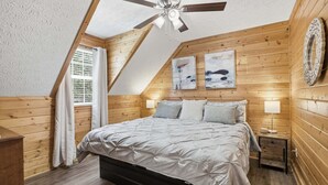 Un dormitorio con techo inclinado, paredes de madera, una cama con cabecera, dos lámparas de noche y una obra de arte en la pared.