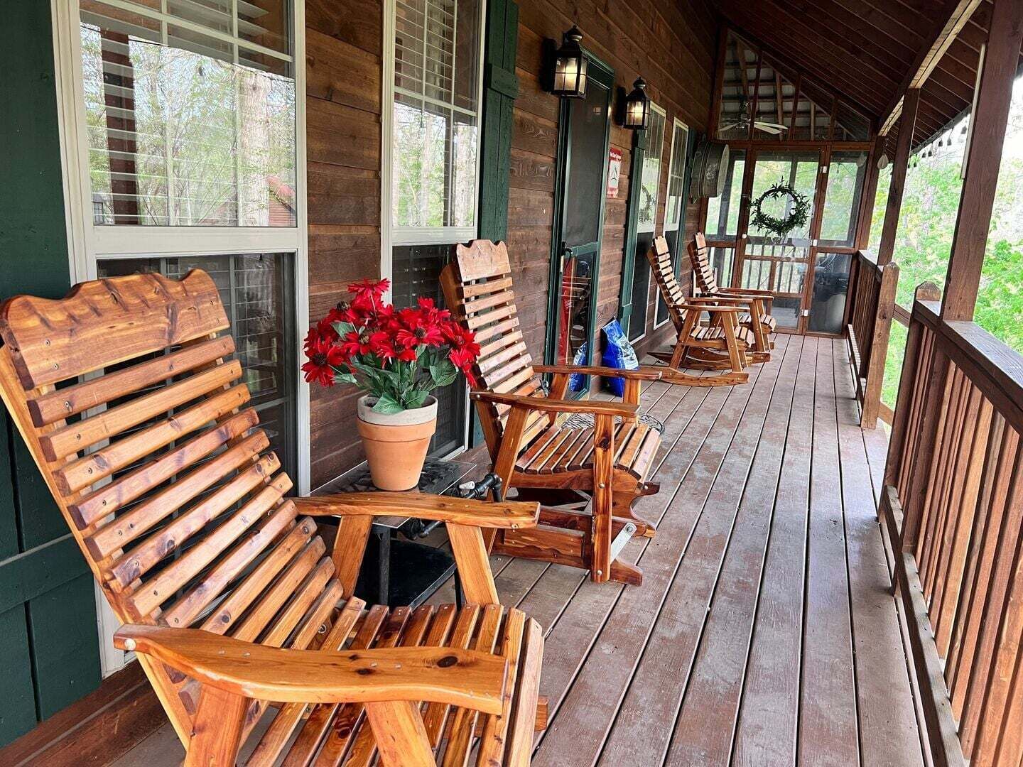 A wooden porch with several rocking chairs and a potted plant.