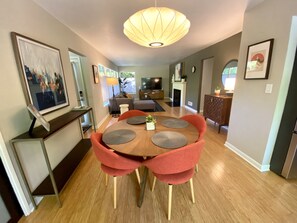 Un espace repas moderne avec une table en bois et quatre chaises rouges, un luminaire suspendu et des œuvres d’art accrochées aux murs.