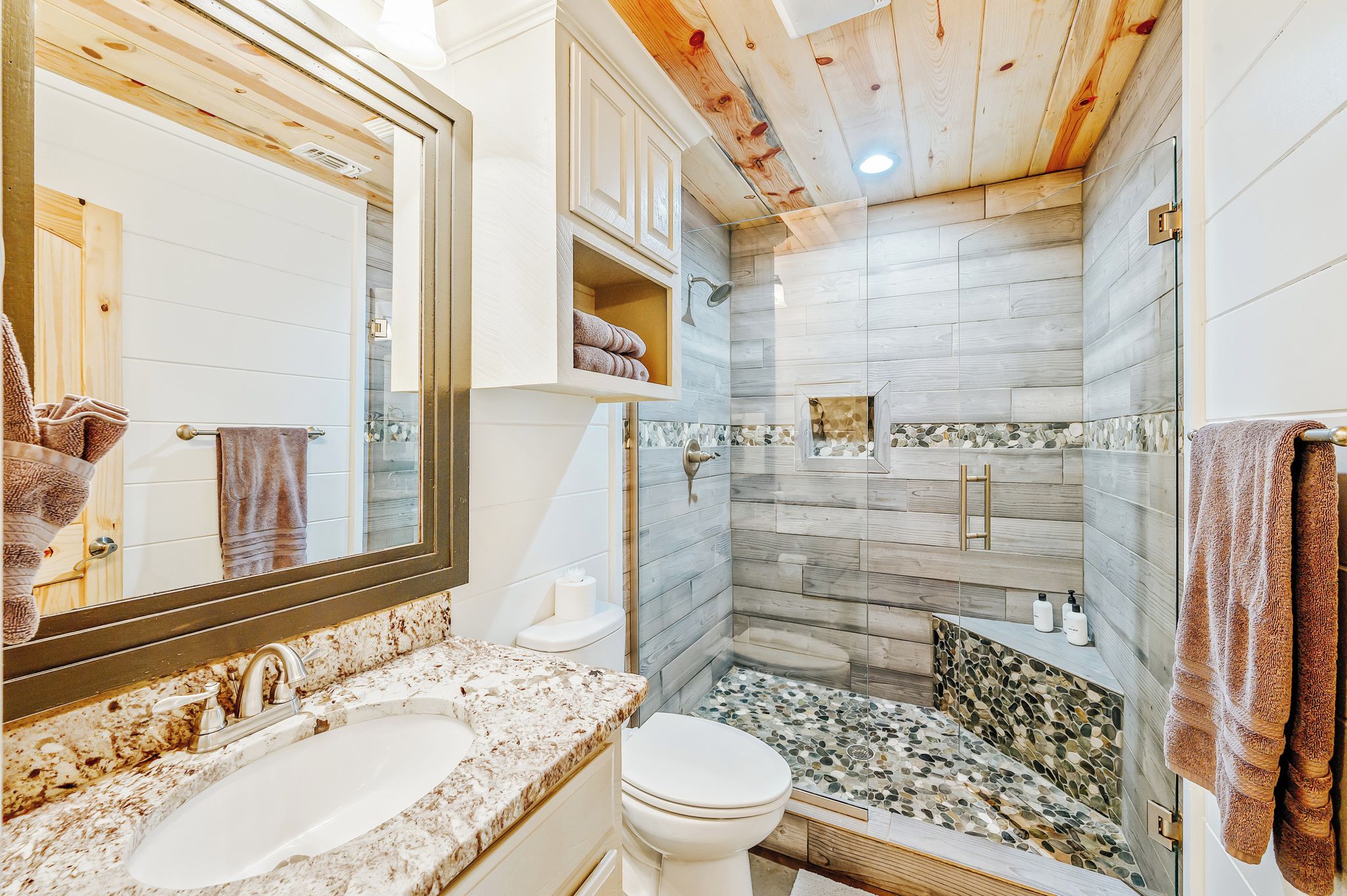 A bathroom with a large mirror, a sink, a toilet, and a shower area with a glass door.