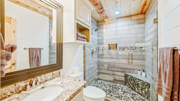 A bathroom with a large mirror, a sink, a toilet, and a shower area with a glass door.