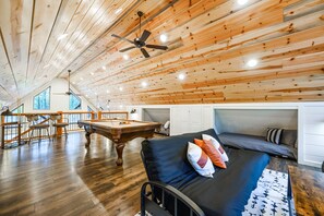 A spacious loft with a pool table, seating area, and a ceiling fan.