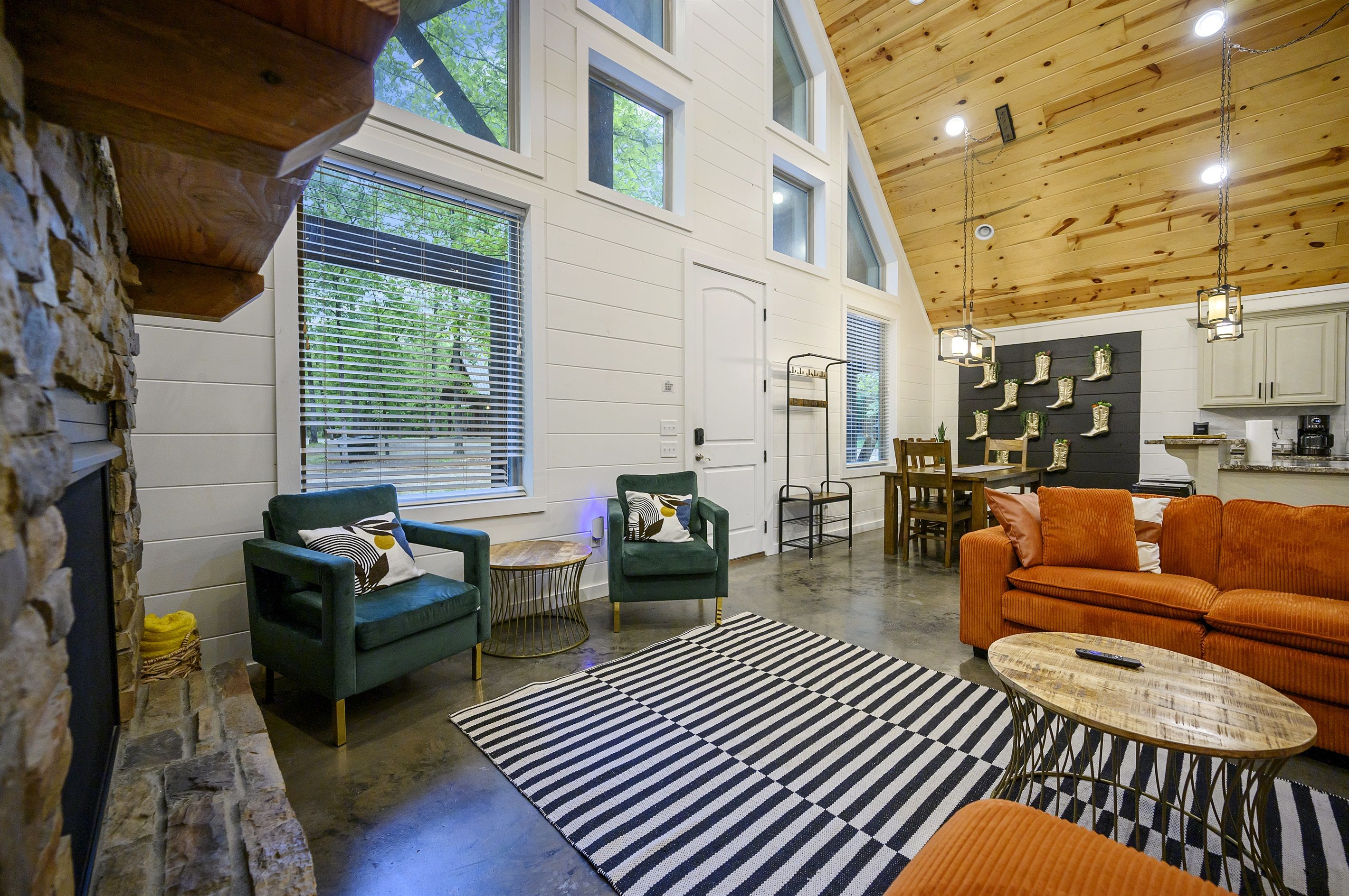 A spacious living area with a stone fireplace, green armchairs, an orange sofa, and a black and white striped rug.
