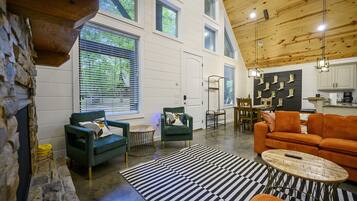 A spacious living area with a stone fireplace, green armchairs, an orange sofa, and a black and white striped rug.