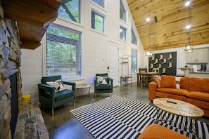 A spacious living area with a stone fireplace, green armchairs, an orange sofa, and a black and white striped rug.