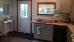 A compact kitchen with a sink, a window, and a clock on the wall.