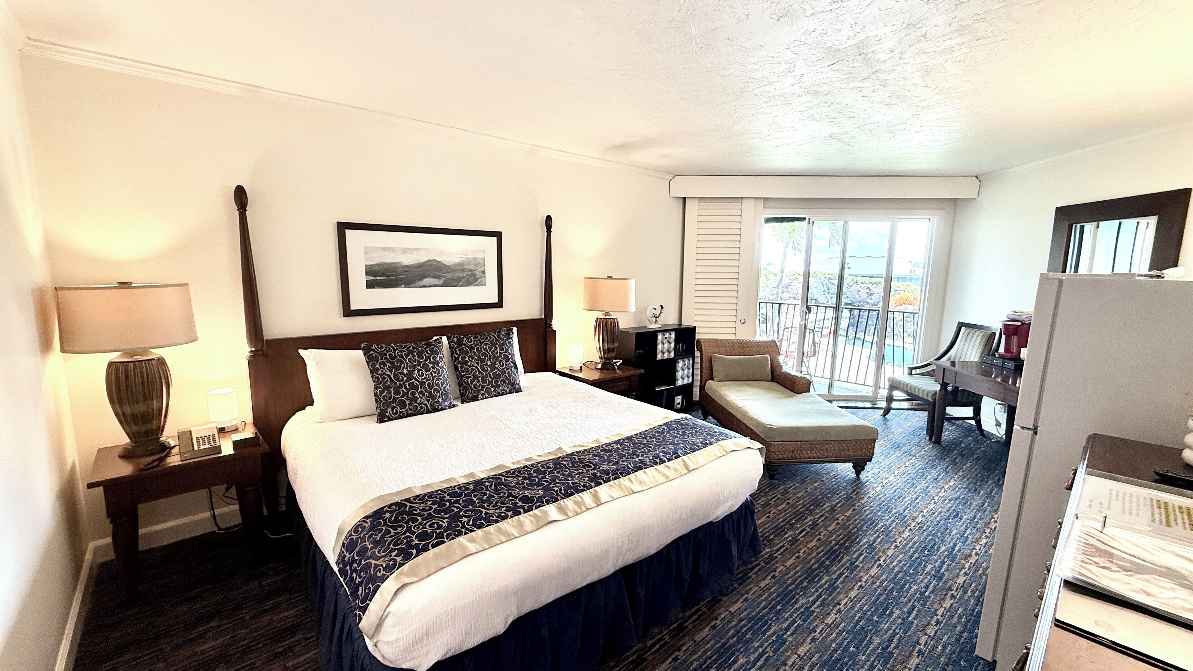 A hotel room with a large bed, a desk, a chair, and a balcony with a view.