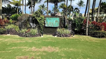 A sign for Kauai Beach Resort surrounded by tropical landscaping and palm trees.