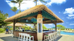 A thatched-roof bar area with outdoor seating, a pool, and palm trees in the background. - Kauai Beach Resort, Top Floor, Pool View (Kauai)