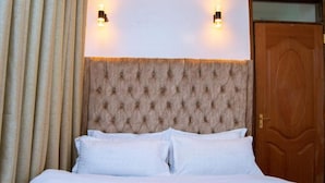 A bed with a tufted headboard, two wall-mounted lights, and a wooden door. - Sandalwood Suites Nakuru (Nakuru)