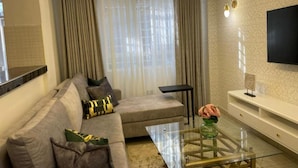 A modern living room with a sofa, a glass coffee table, and a TV mounted on the wall. - Sandalwood Suites Nakuru (Nakuru)
