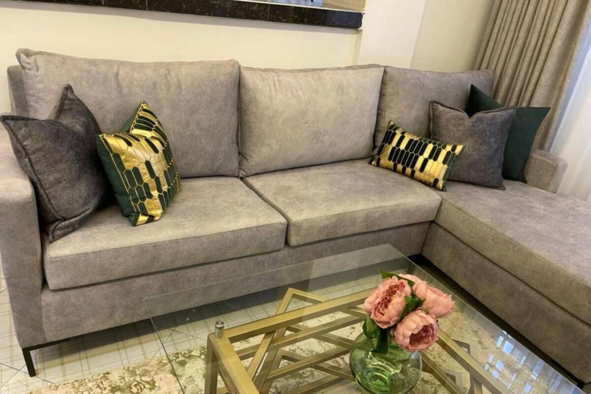 A grey sofa with patterned cushions, a glass coffee table with a vase of flowers, and a tiled floor.