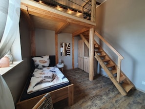 Une chambre à coucher aménagée dans un espace en hauteur, avec un lit en bois, une table de chevet, un miroir et un escalier.