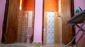 A bathroom with a pink toilet, patterned tiles, and a wooden door. - Fountain Apartments (Naivasha)