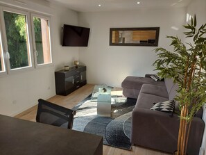 A modern living room with a sofa, a coffee table, a TV mounted on the wall, and a large window.