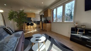 A modern living room with a sofa, two round tables, and a large window providing natural light.