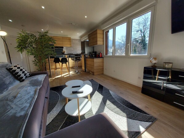 A modern living room with a sofa, two round tables, and a large window providing natural light.