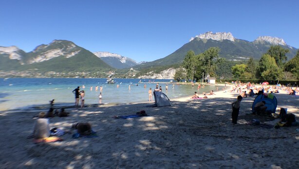 A beach with people sunbathing and swimming, tents set up, and mountains in the background.