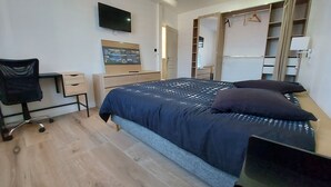 A modern bedroom with a bed, a desk, a chair, a TV, and a wardrobe.