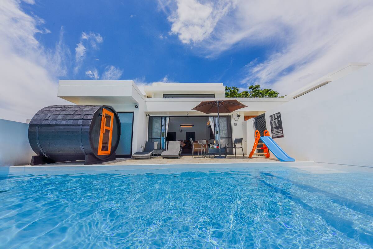A modern pool area with a clear blue sky, a large cylindrical water feature, and a slide.