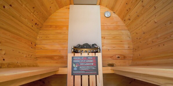 A sauna with wooden walls and benches, a thermometer, and a sign with instructions in Japanese.