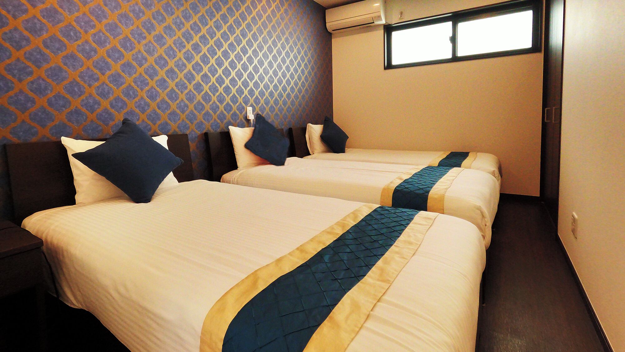 A hotel room with two beds, a patterned wall, and a window.