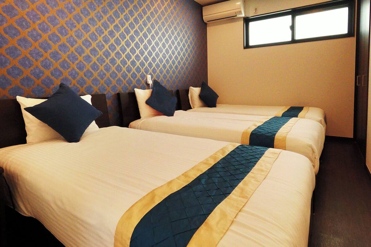 A hotel room with two beds, a patterned wall, and a window.