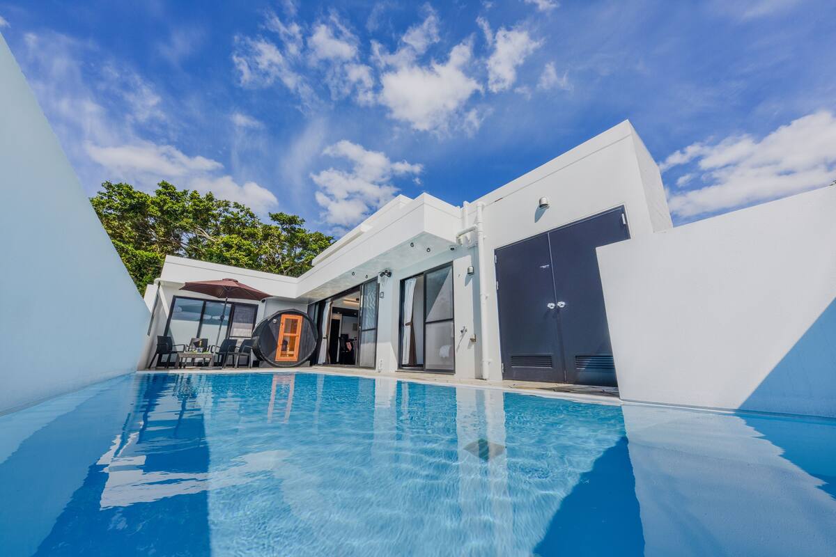 A modern poolside area with a clear blue sky, a pool, and a building with large windows and a garage door.