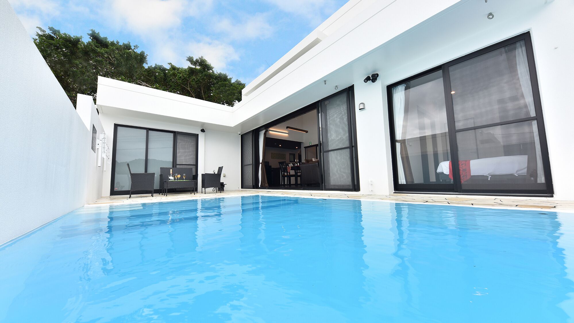 A modern poolside area with a clear blue pool, large sliding glass doors, and outdoor furniture.