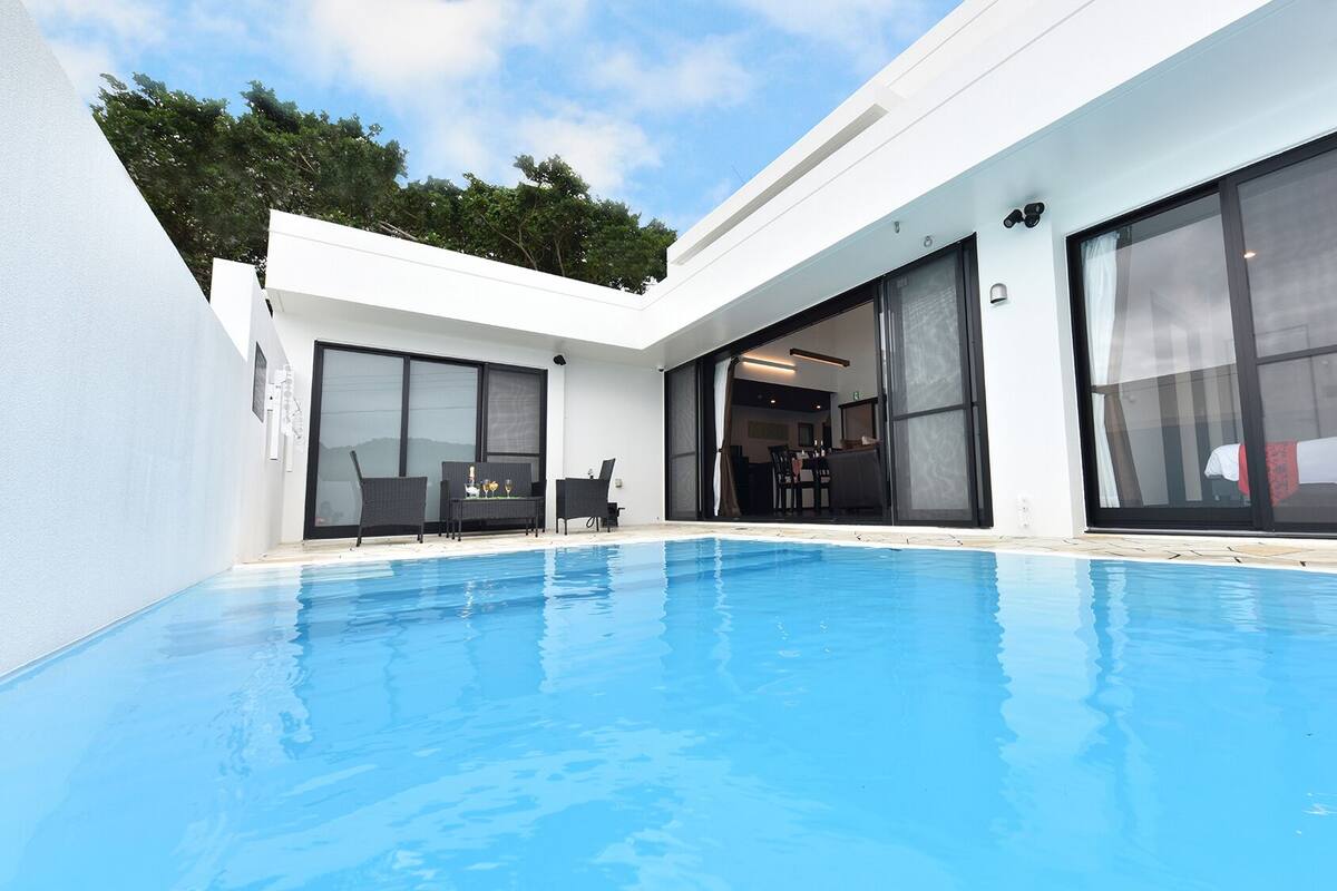 A modern poolside area with a clear blue pool, large sliding glass doors, and outdoor furniture.
