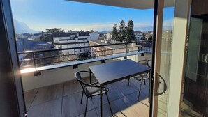 Ein Balkon mit Tisch und Stühlen, der auf eine Stadtansicht mit Gebäuden und Bäumen blickt.