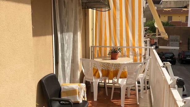 A balcony with a tiled floor, a table with chairs, a potted plant, and a striped curtain.