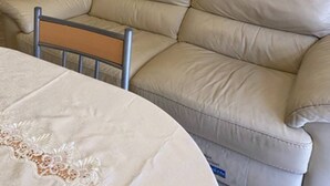 A beige leather sofa in a room with a white wall, a wooden door, and a small table with a white tablecloth.
