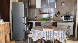 A compact kitchen with a refrigerator, microwave, and sink. There is a dining table with chairs and a sofa in the living area.