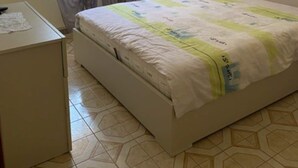 A bedroom with a bed, a bedside table, a window with curtains, and a wall-mounted picture.