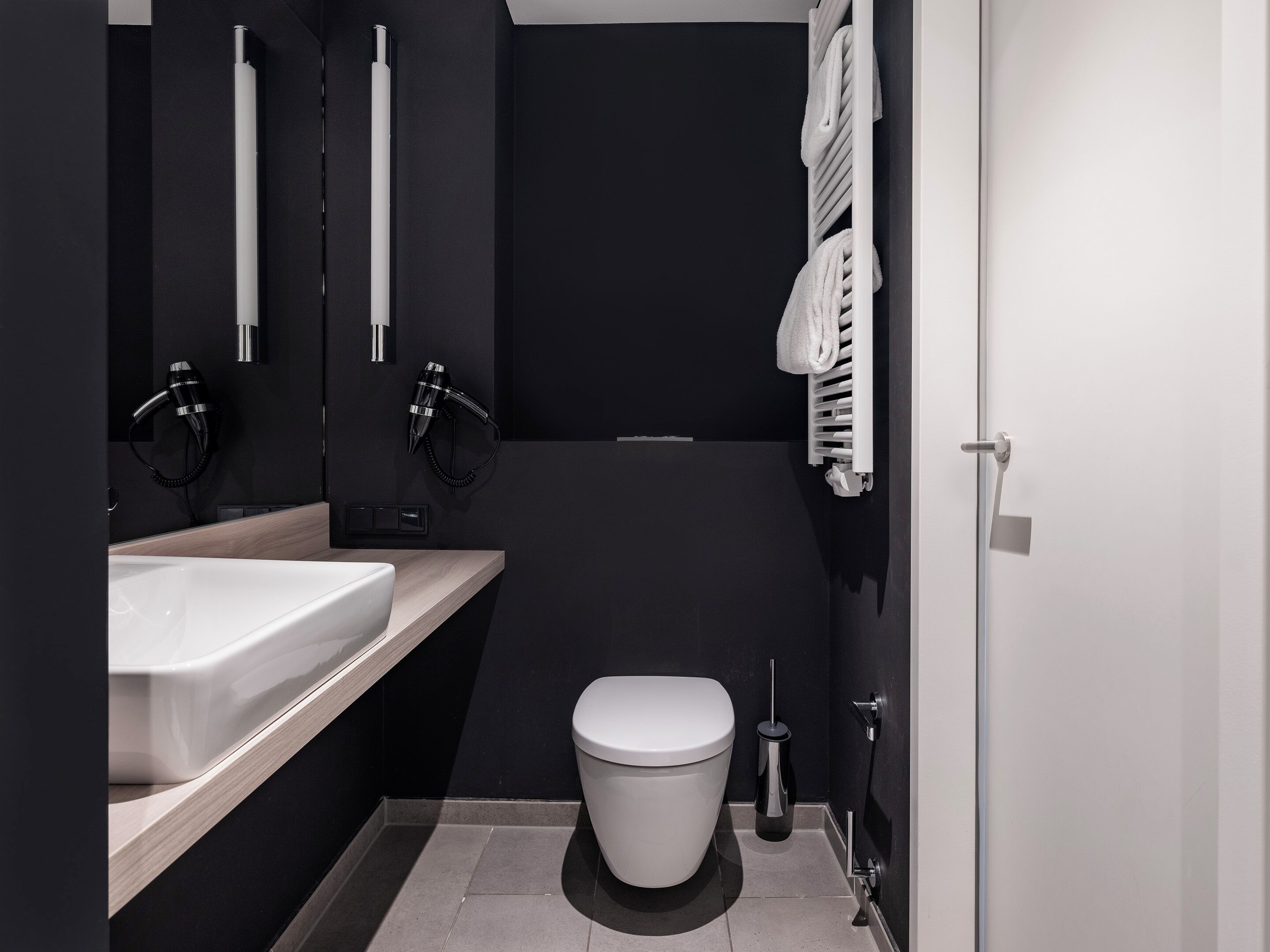 Um banheiro moderno com pia branca, porta-toalhas preto e vaso sanitário.