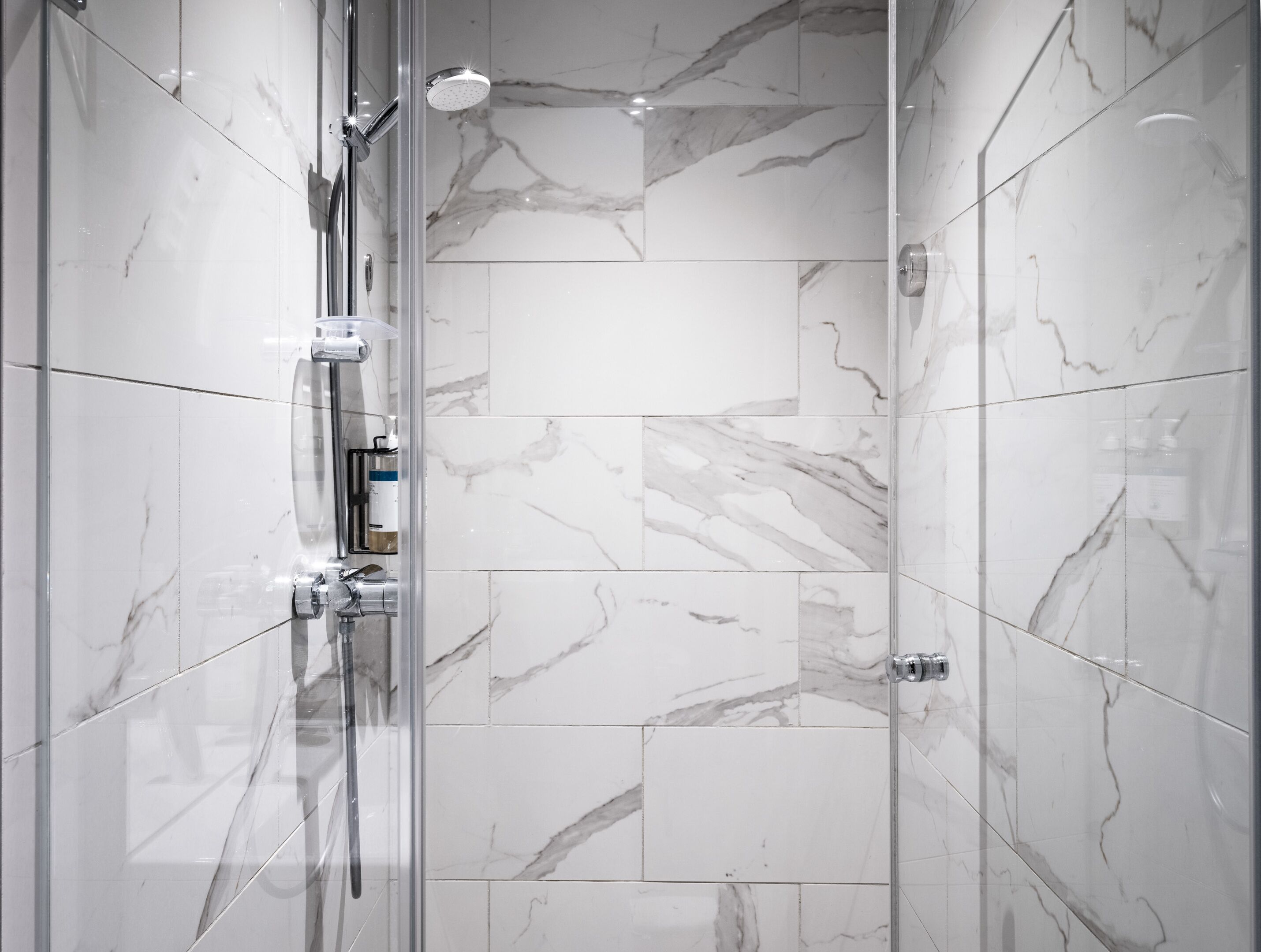 Une douche moderne dotée d’une porte en verre, de carreaux de marbre et d’un pommeau de douche à main.