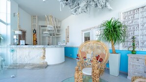 A modern living room with a glass coffee table, wicker furniture, a large potted plant, and a white cabinet with decorative items. - Kouros Home and Suites (Rhodes)