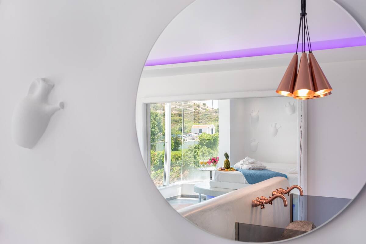 A modern bathroom with a large mirror, a white sink, and a copper faucet.