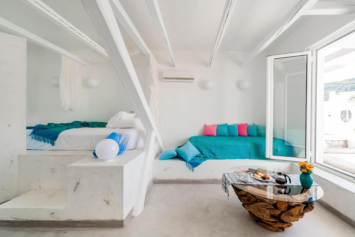 A modern, white-themed bedroom with a bed, a seating area with a table, and a large window.