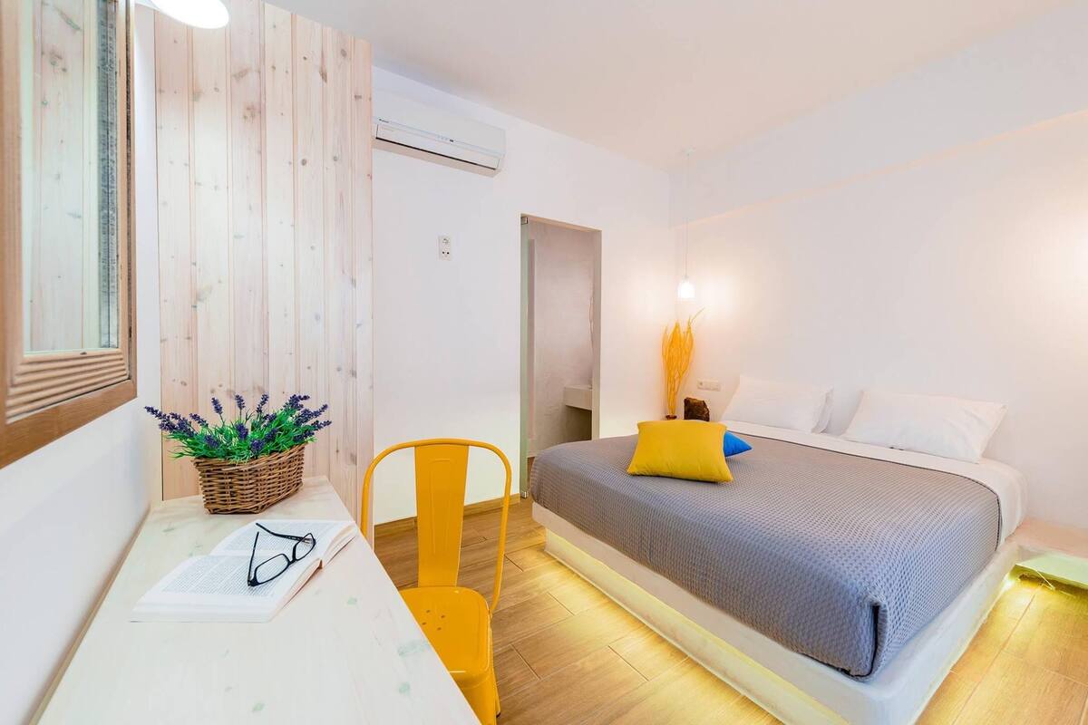 A bedroom with a bed, a desk with a chair, a window, and a wall-mounted air conditioner.