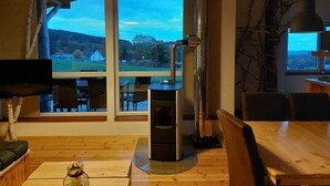 A cozy room with a large window, a wood-burning stove, and a view of a rural landscape.