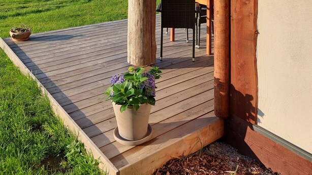 A wooden deck with a potted plant, a table, and chairs.